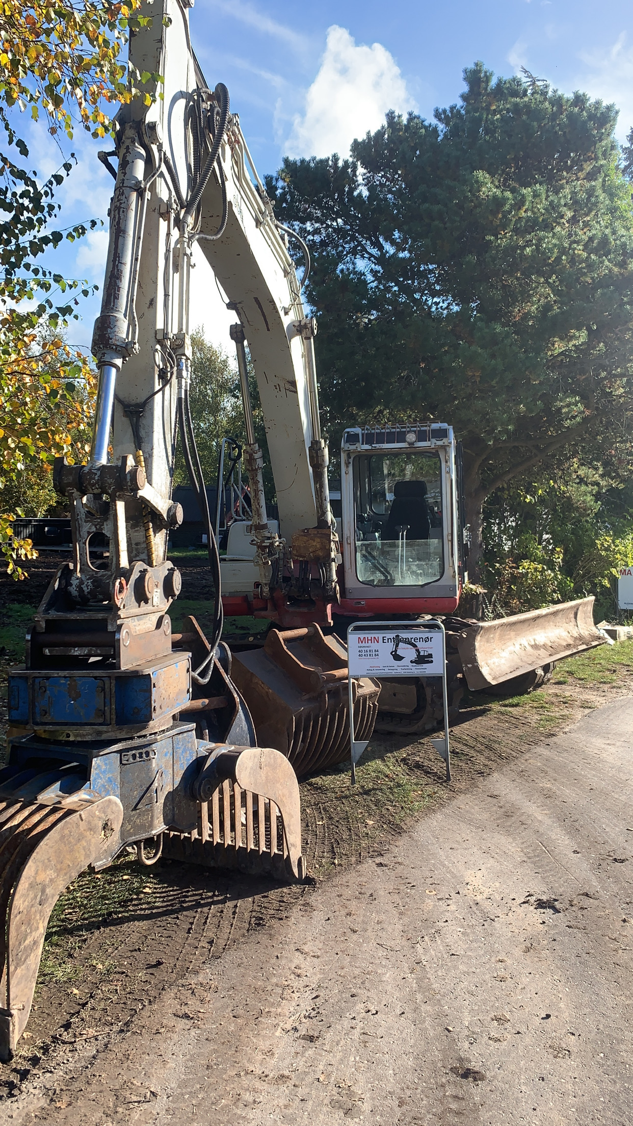 Nedrivningsmaskine foran skilt fra MHN Entreprenør